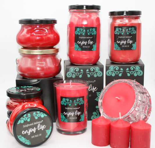 A collection of Dickens Christmas scented candles in various sizes and packaging, with a prominent red candle in the foreground and a label that reads 'Enjoy Life'. The candles are displayed against a white background.